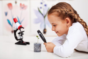 photo of a young girl looking at a plant through a magnifying glass